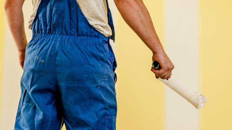 Painter with Painting brush standing in front of a wall with yellow and white strips