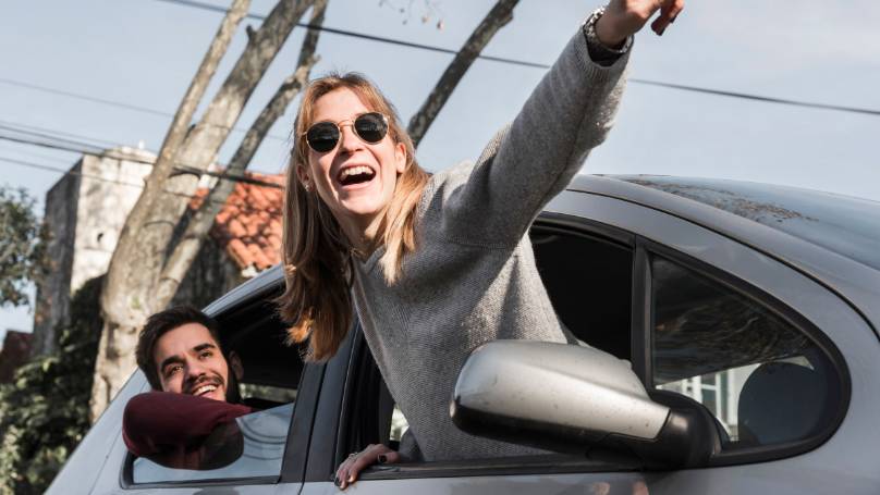 Two people hanging out of the window of a parked car and pointing into the distance