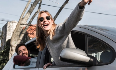 Two people hanging out of the window of a parked car and pointing into the distance