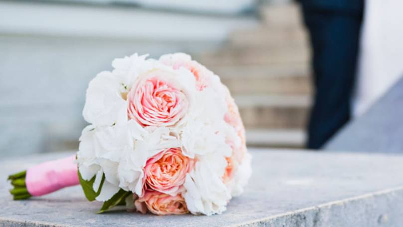 Wedding bouquet with pink and white roses, sat on stone stair bannister, bride & groom in distance