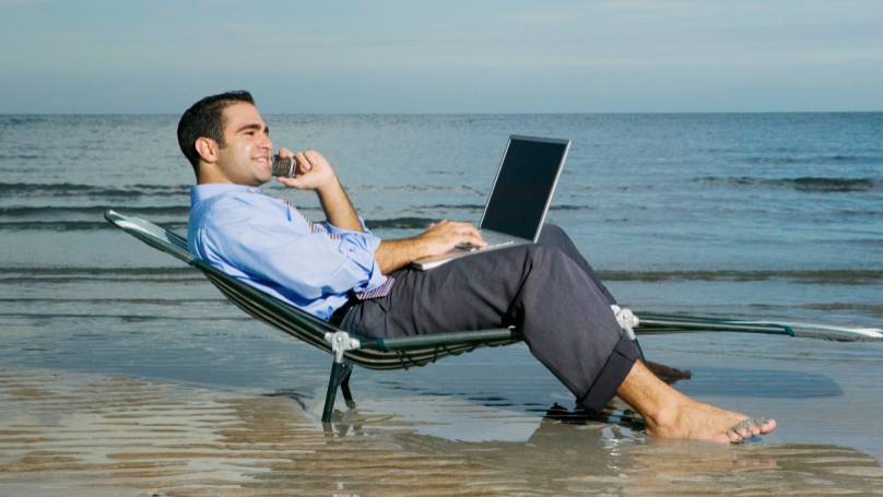 man sitting on the beach with his laptop