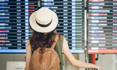 Woman wearing hat and backpack at airport looking a departure board at the airport