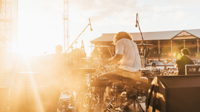 Drummer and band playing music to a crowd with sun in background