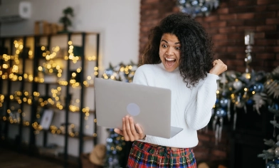a person excitedly looking at an open laptop in a room decorated for christmas